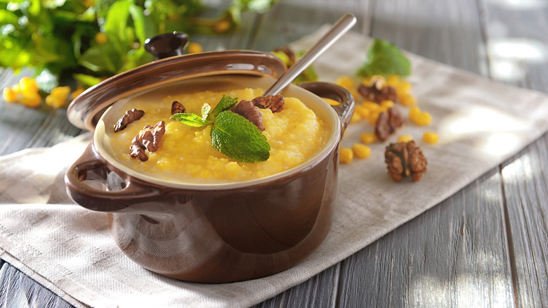 A pot of cornmeal mush topped with greenery and walnuts on a linen napkin