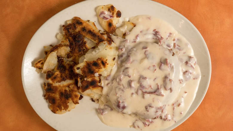 A white plate of creamed chipped beef and home fries on an orange surface