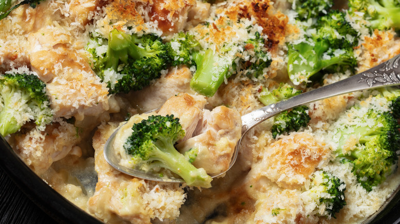 close-up shot of a spoon digging into a cheesy chicken and broccoli casserole, topped with crumbs