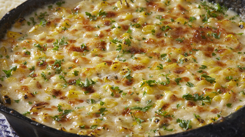 close-up of a cheesy corn casserole in a cast iron pan, brown and bubbling from the oven