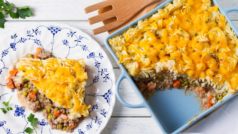 a portion of shepher'd pie on a patterned plate next to the rest in a serving dish