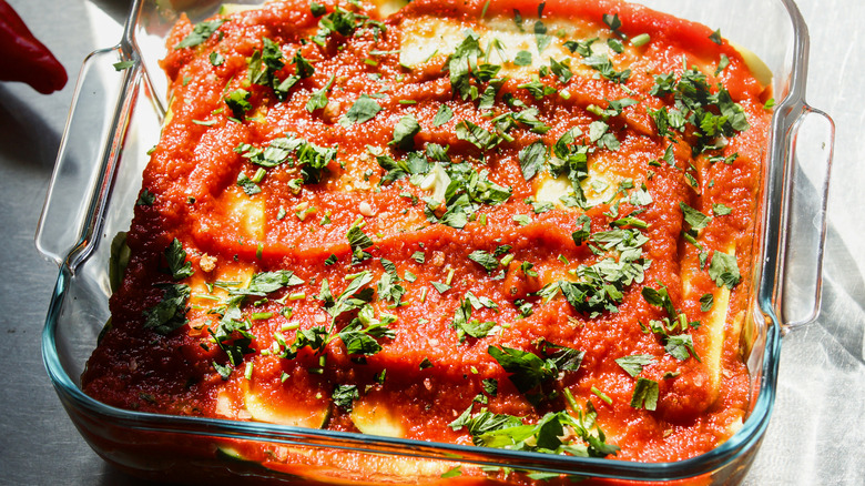 moody shot of a casserole in a kitchen, topped with tomato sauce, ready to go into the oven