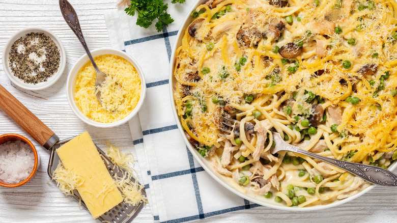 overhead shot of turkey tetrazzini in a baking dish, styled with ingredients on a white wood background