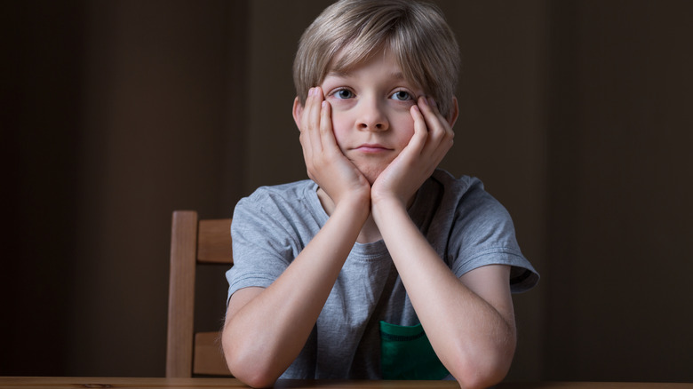 A young boy sits with elbows on the table