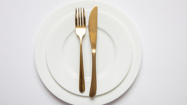 A pair of plates with a gold knife and fork