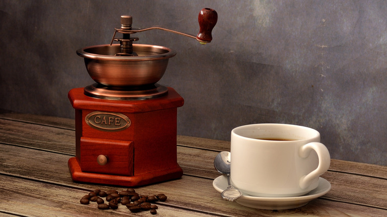 A manual coffee grinder next to a cup of coffee