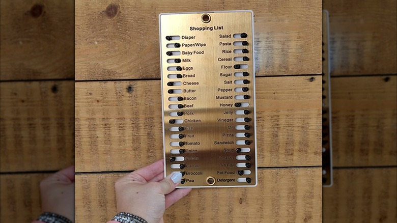 A hand holds a metal grocery list