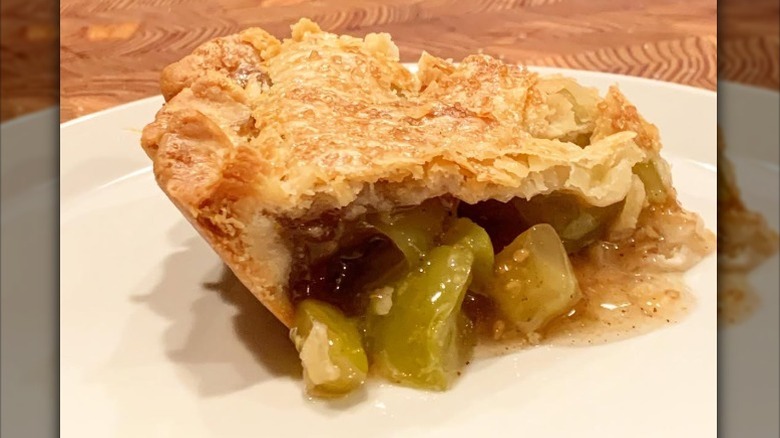 A slice of green tomato pie on a white plate that is placed on a wooden table
