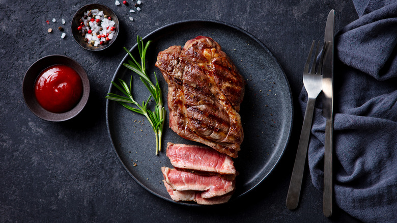 Rare steak on a black plate, with salt and ketchup next to it