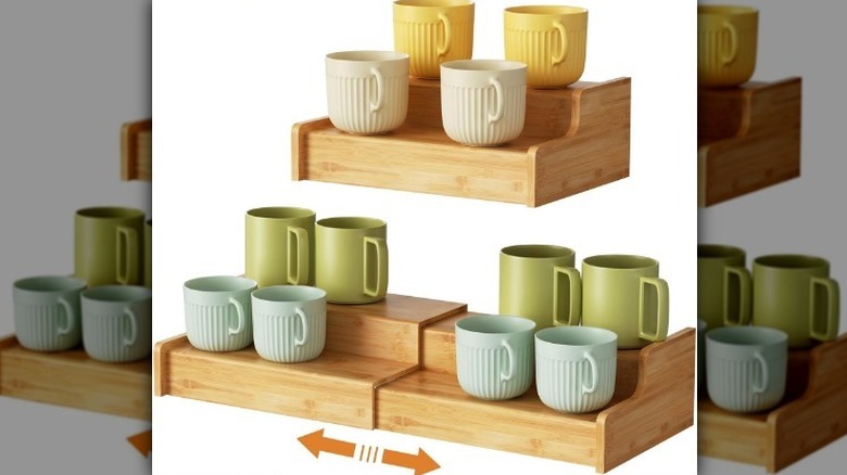 Adjustable multi level shelf on white background with pale blue, sage green, cream, and yellow mugs.