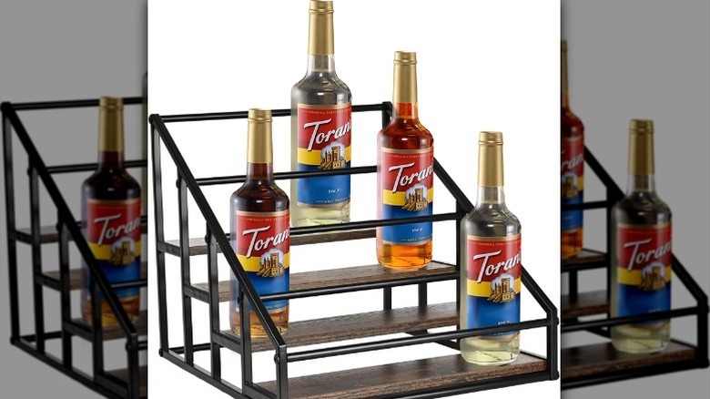 Torani syrup bottles sit on a tiered rack against a white background