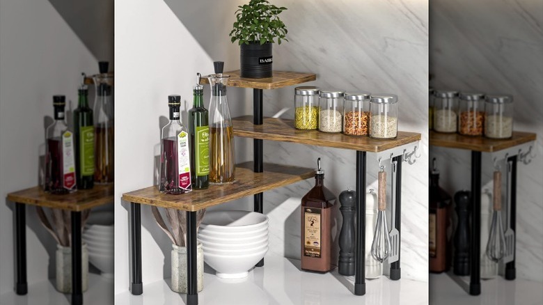 Three-tier shelf organizer made of wood shelves and black legs on counter with assorted bottles, jars, and other kitchen items.