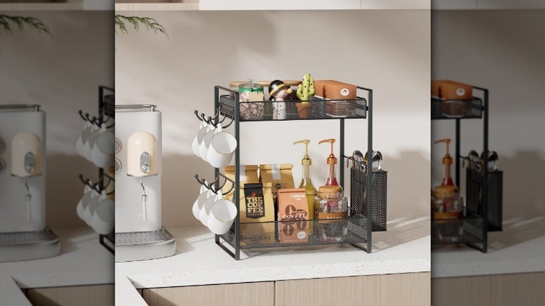 Metal two tier rack on counter with coffee bags, syrup pumps, mugs, and other kitchen trinkets on it.