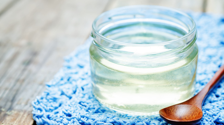 A jar of sugar syrup sits on a blue mat, with a wooden spoon next to it