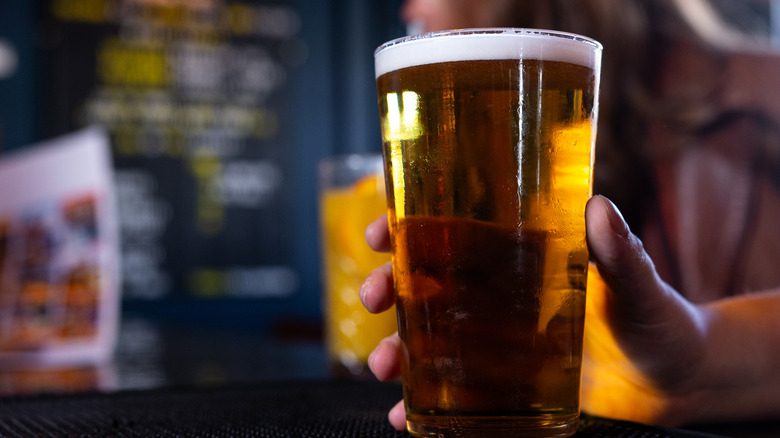 A hand holds a glass of beer at a bar