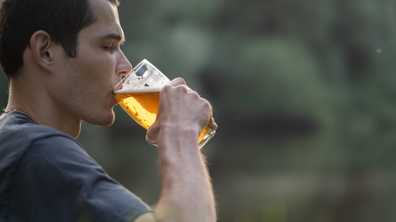 A man wearing a grey T-shirt takes a sip of beer