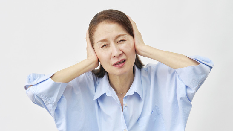 An older woman covers her ears with her hands