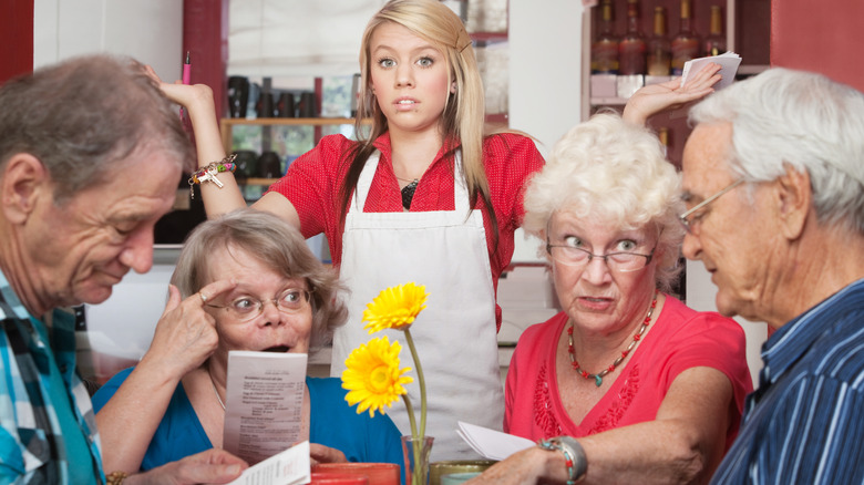 A young server is annoyed while a group of older restaurant customers argue