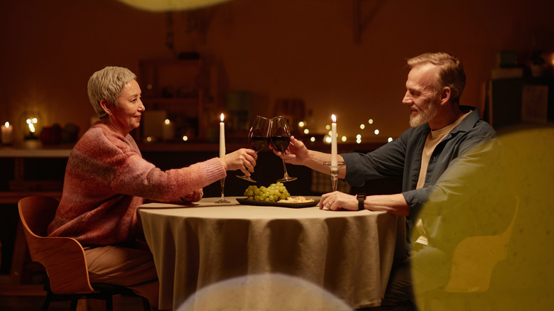 An older couple clink wine glasses and eat in a restaurant