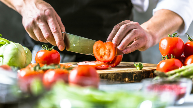 A person slices a tomato while prepping ingredients