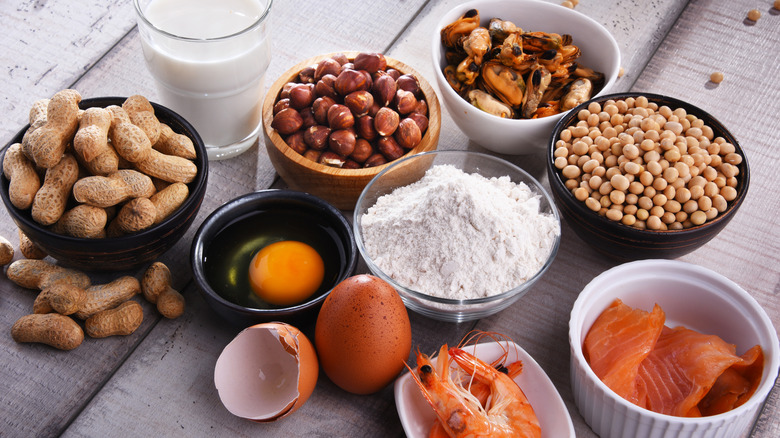Many common food allergens on a wooden table including dairy, eggs, nuts, fish, and shellfish