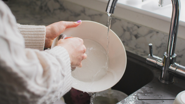 Close up of a person in a white sweater washing a dish in the sink