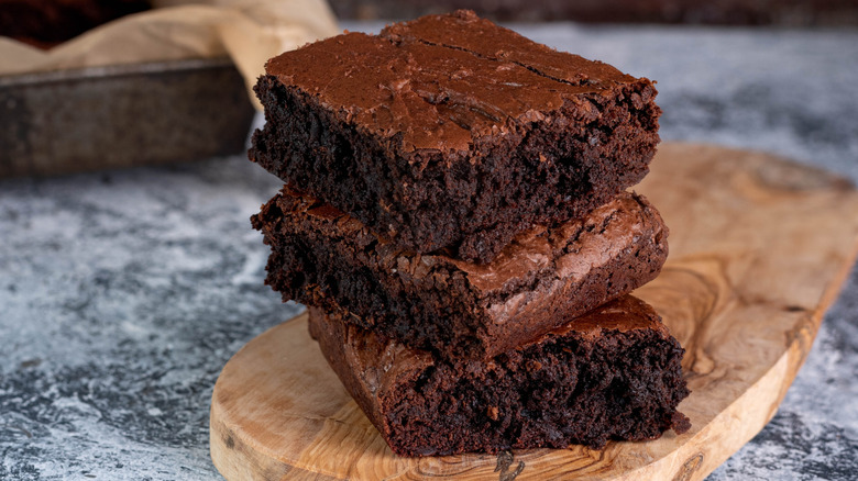 Three brownies stacked on top of each other on a wooden board sitting on a marble surface