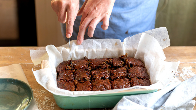 A person cutting brownies while they are still in the baking pan
