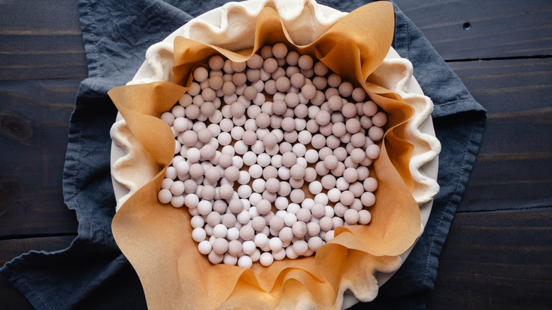 A pie crust lined with parchment and beans for blind baking on a table