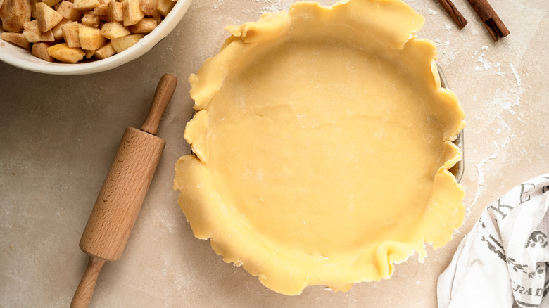 Pie dough lined in a pan with a lot of overhang on a table