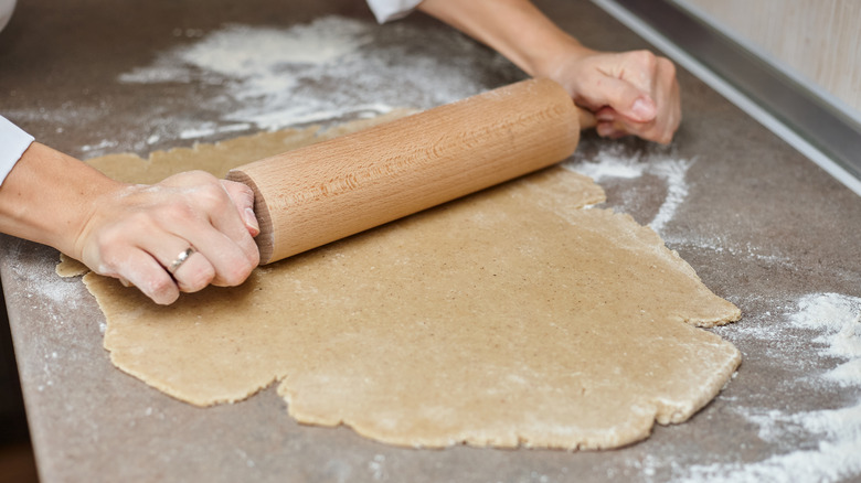 A person rolling out dough with a large rolling pin