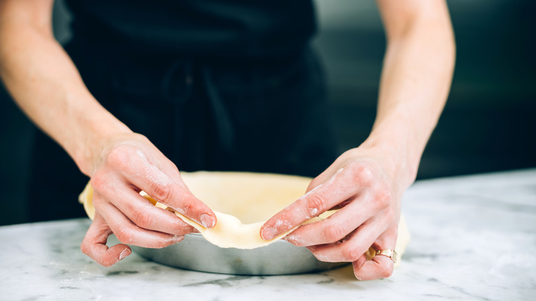 A baker stretching pie dough that's lined inside a pan