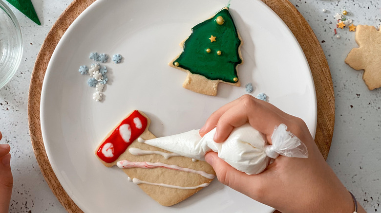 A person piping royal icing on a stocking shaped sugar cookie