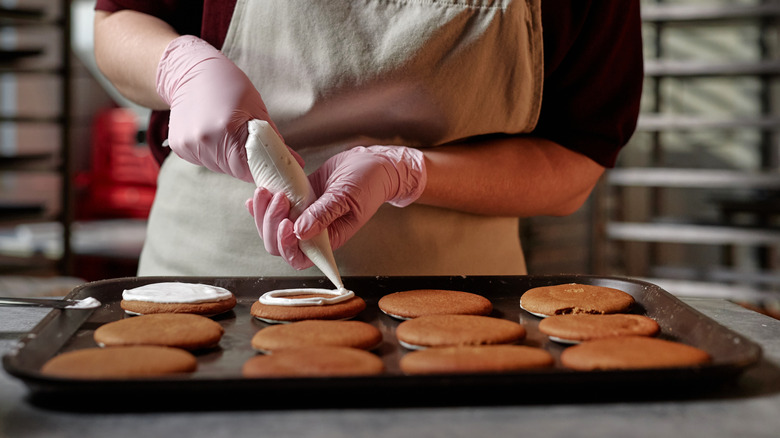 A person piping royal icing on cookies