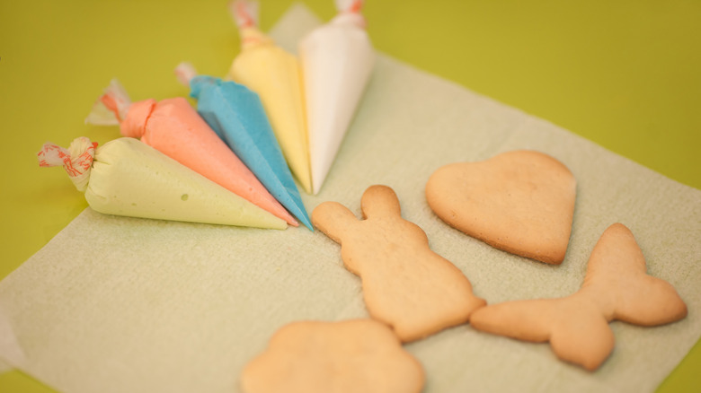 Four sugar cookies and five piping bags filled with different colored icings on a table