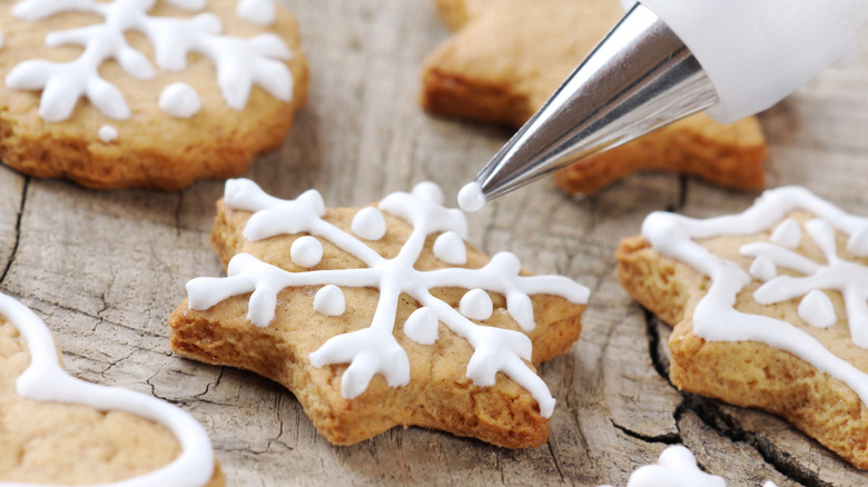 Royal icing being piped on a sugar cookie with other cookies on the side