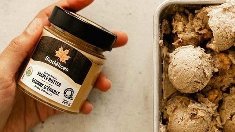 A jar of Biodélices Organic Maple Butter in a woman's hand, next to a dish with scoops of ice cream
