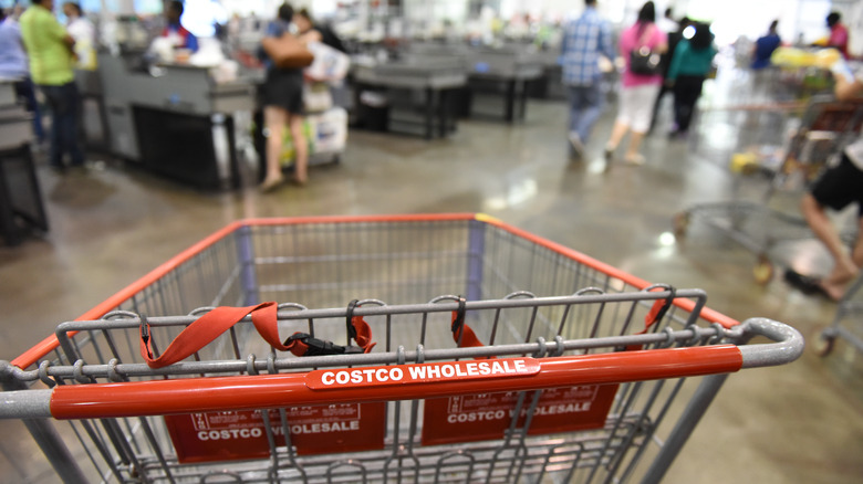 An empty Costco shopping cart with a busy checkout area in the background