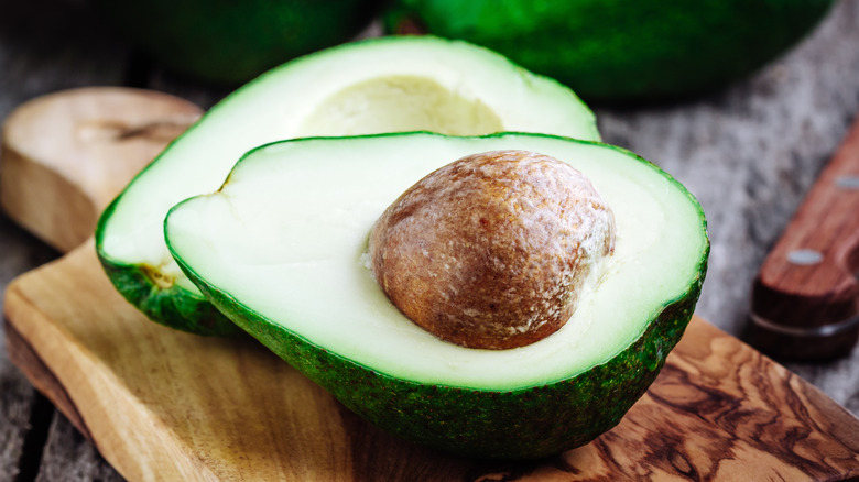 An avocado cut in half and laying on a wooden cutting board