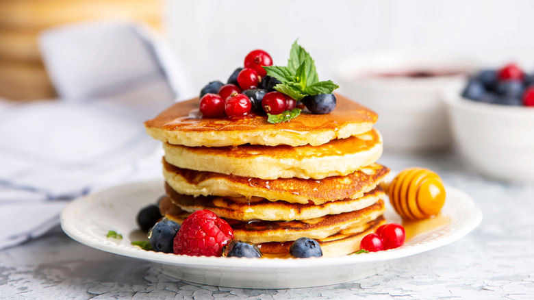 A stack of pancakes on a white plate with fresh berries and honey