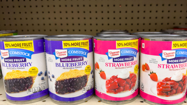 Two cans each of blueberry and strawberry pie filling on a shelf