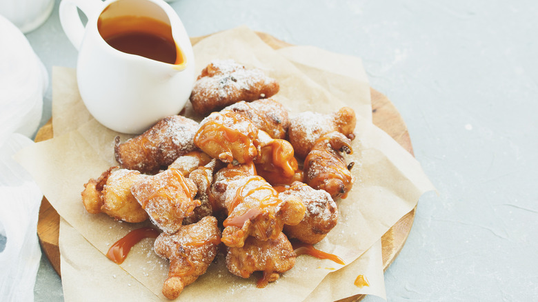 Apple fritters on a wooden plate with a bowl of caramel sauce on the side