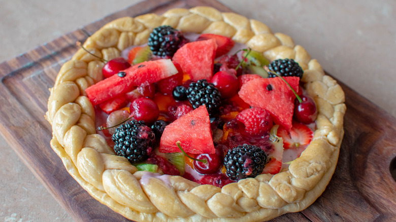 A dessert pizza topped with fruits placed on a wooden board