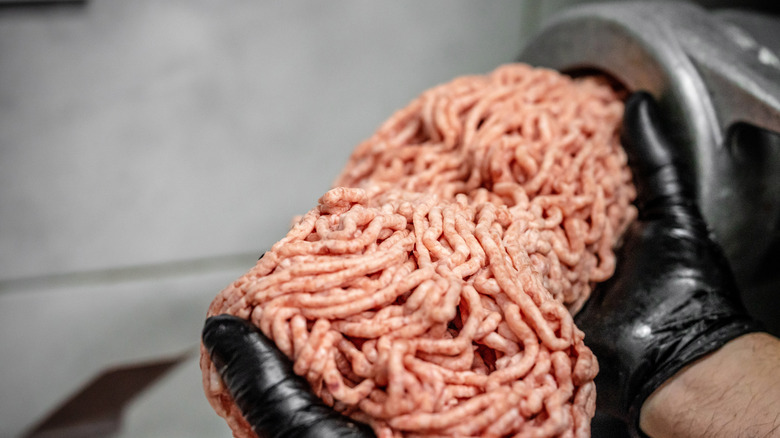 A person holding freshly ground meat as it comes out of a grinder