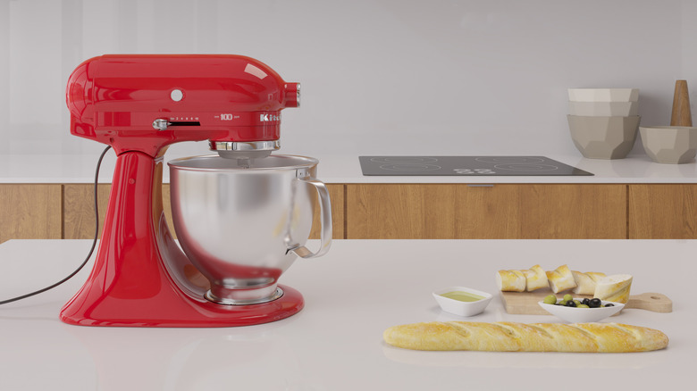 A red KitchenAid mixer on a marble table with bread on the side