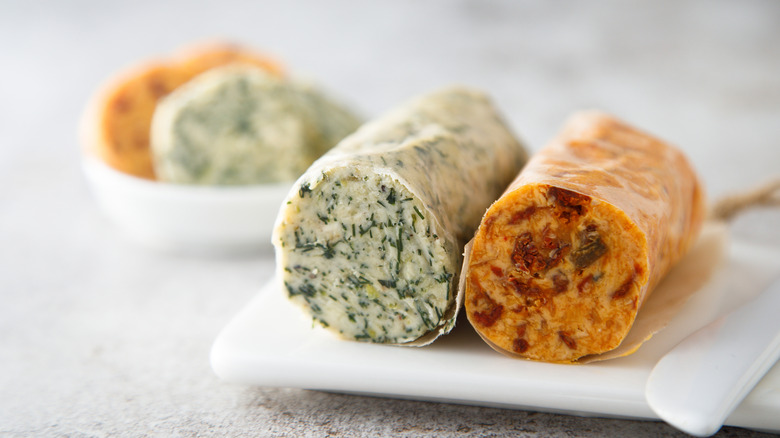 Two logs of flavored butters on a white plate