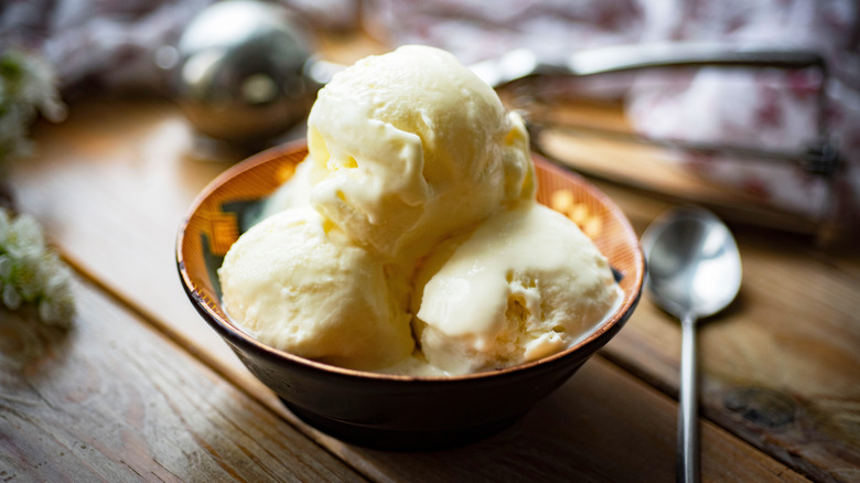 Three scoops of vanilla ice cream in a bowl on a wooden table with a spoon