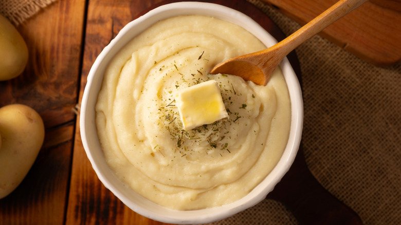 A bowl full of mashed potatoes topped with butter and herbs on a wooden table