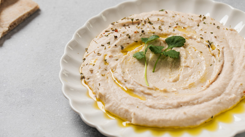 Hummus topped with fresh cilantro in a white dish on a white table