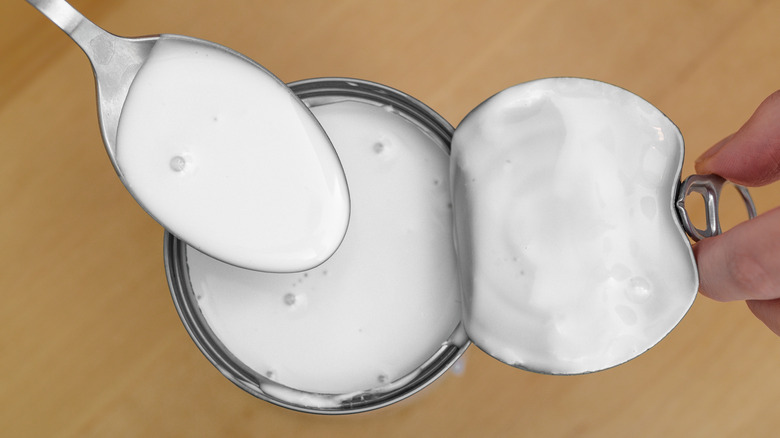 A person holding the top of an opened can of coconut milk and spooning some out